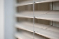 Nahaufnahme eines weißen Raffstore-Lamellenbehangs vor einem Fenster
